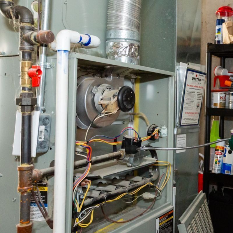 Open furnace cabinet with ducts, wiring, and blower motor inside a utility room.