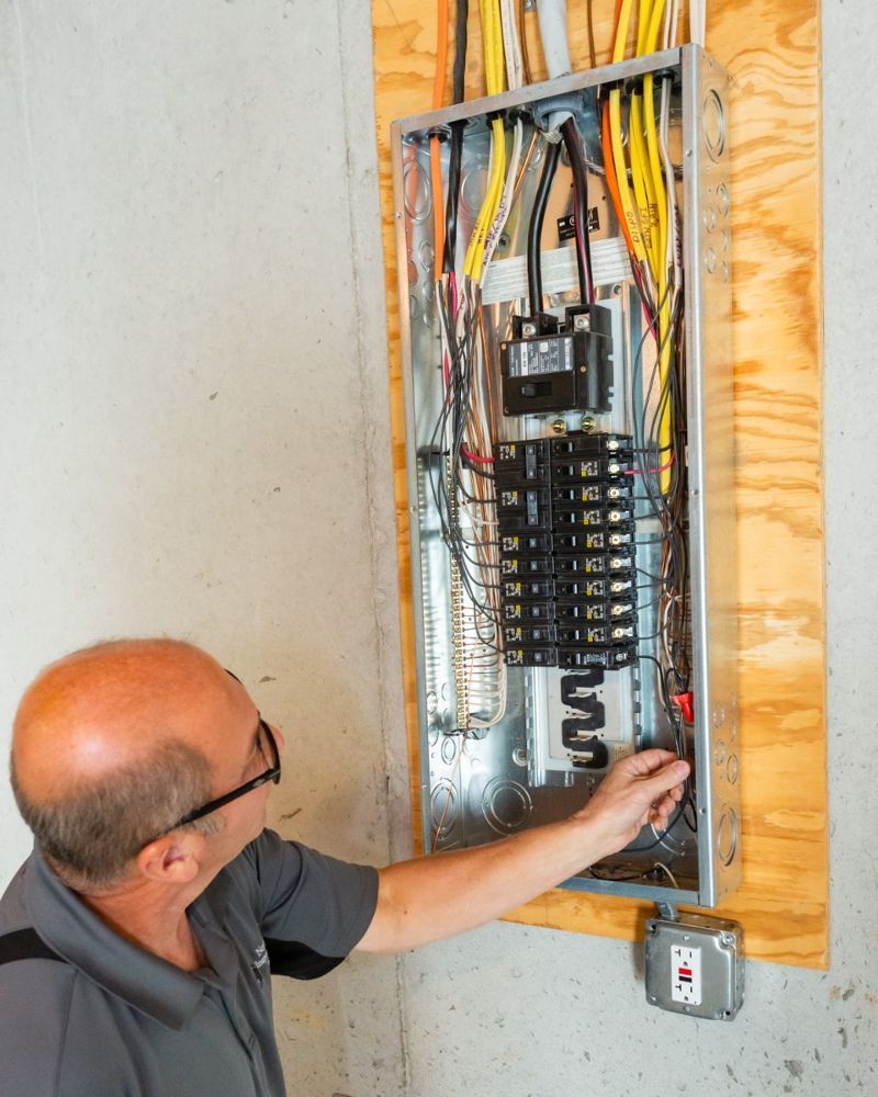 Electrician working inside an open breaker panel with exposed wires and switches
