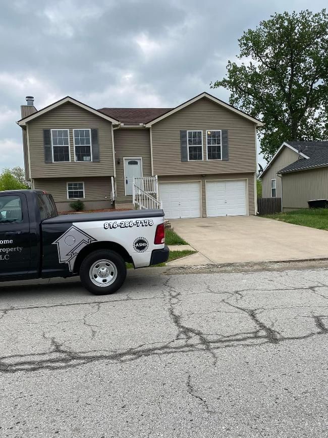 Two-story beige house with double garage on a cloudy street, with a black pickup truck parked in front.