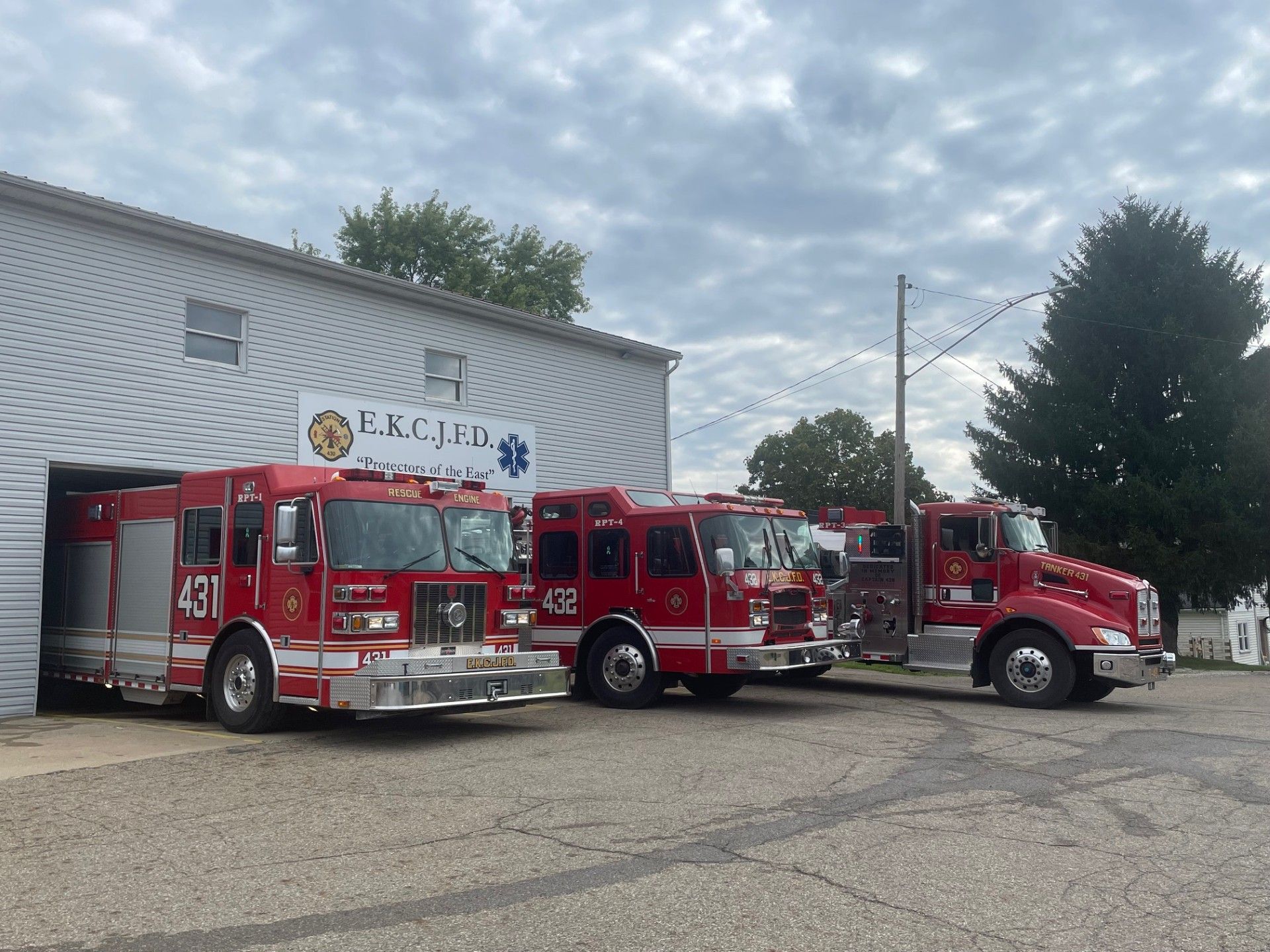 Three red fire trucks parked in front of the EKCAD fire station under a cloudy sky.