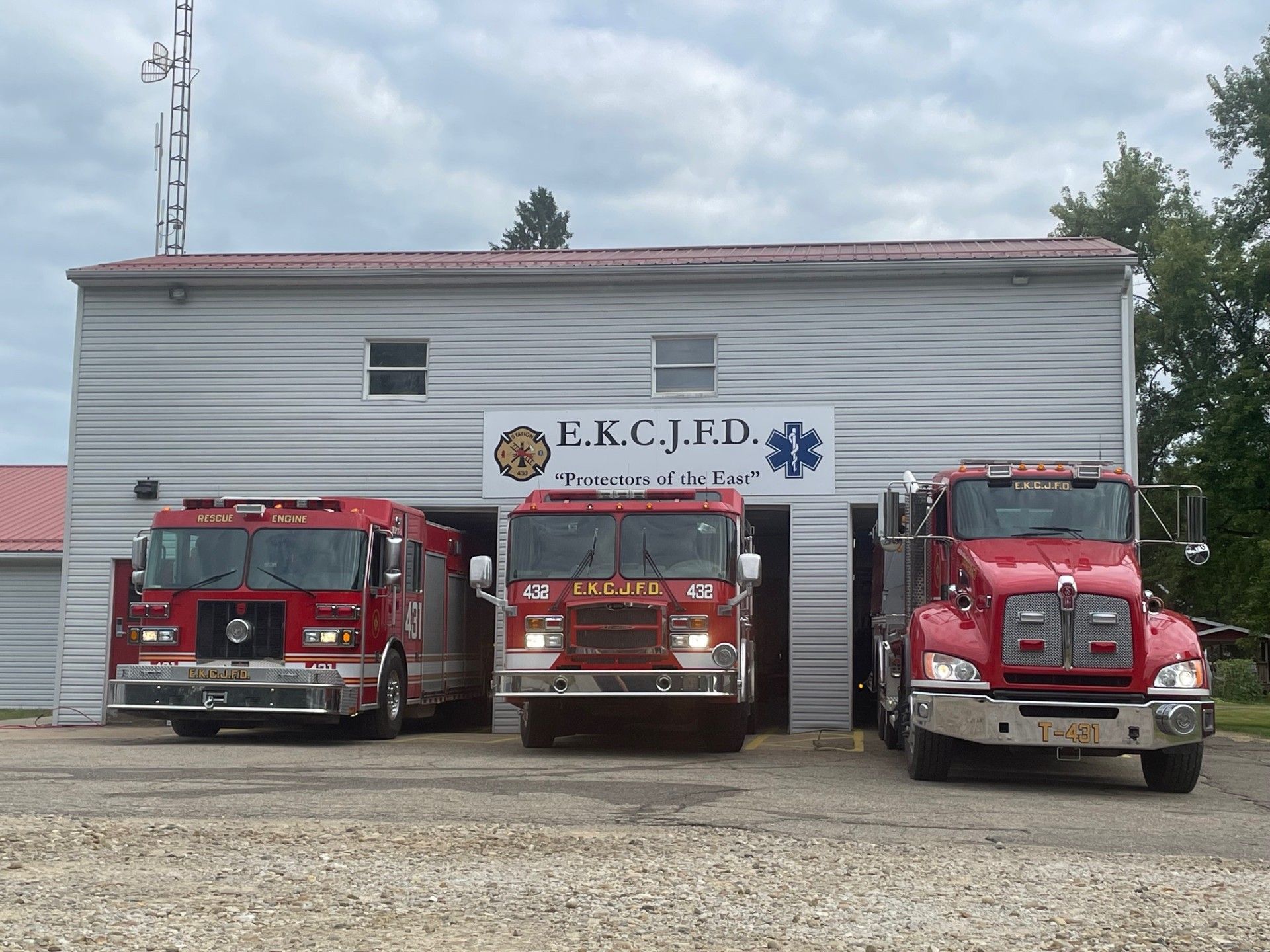 Three red fire trucks parked in front of a fire station with the letters 
