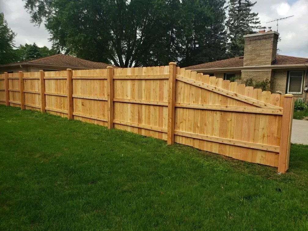 A wooden privacy fence steps down in height toward a suburban house and yard on a sunny day.