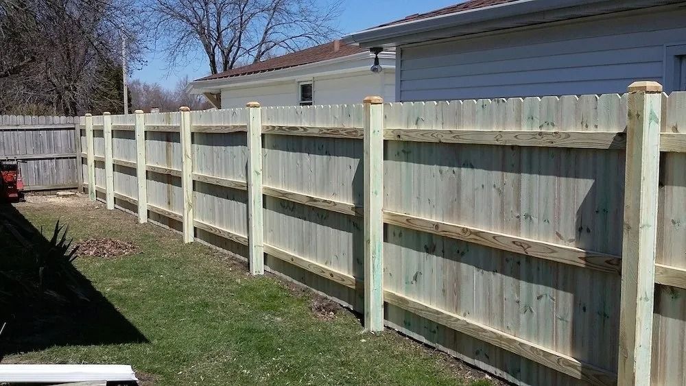 A new wooden privacy fence with vertical slats and three horizontal support rails stands in a grassy backyard.
