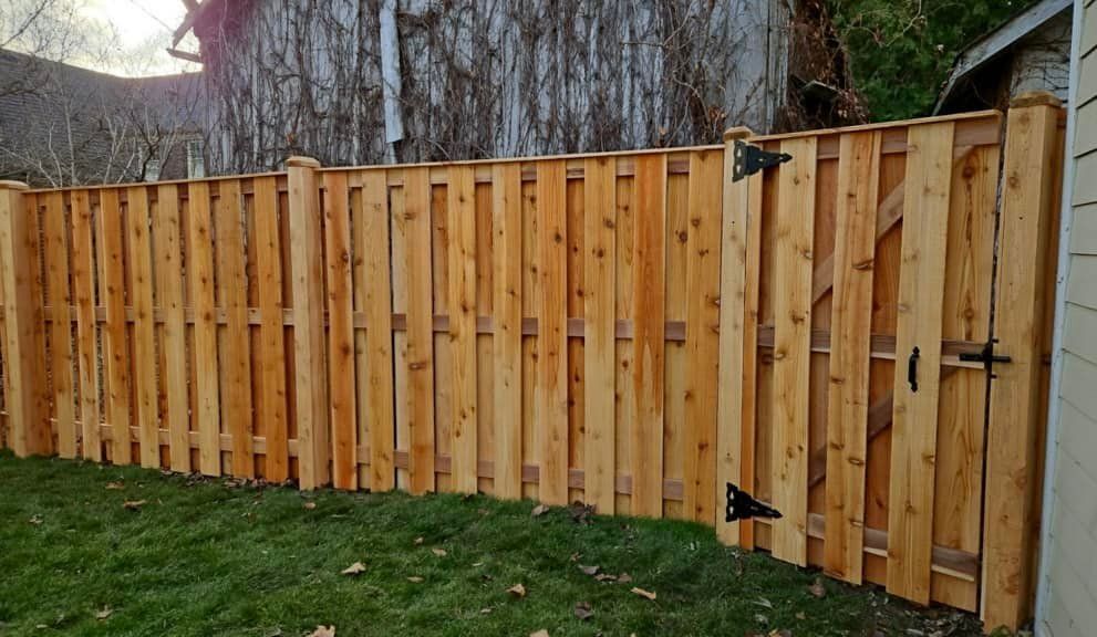 A new cedar wood privacy fence with a matching gate installed along a green lawn.