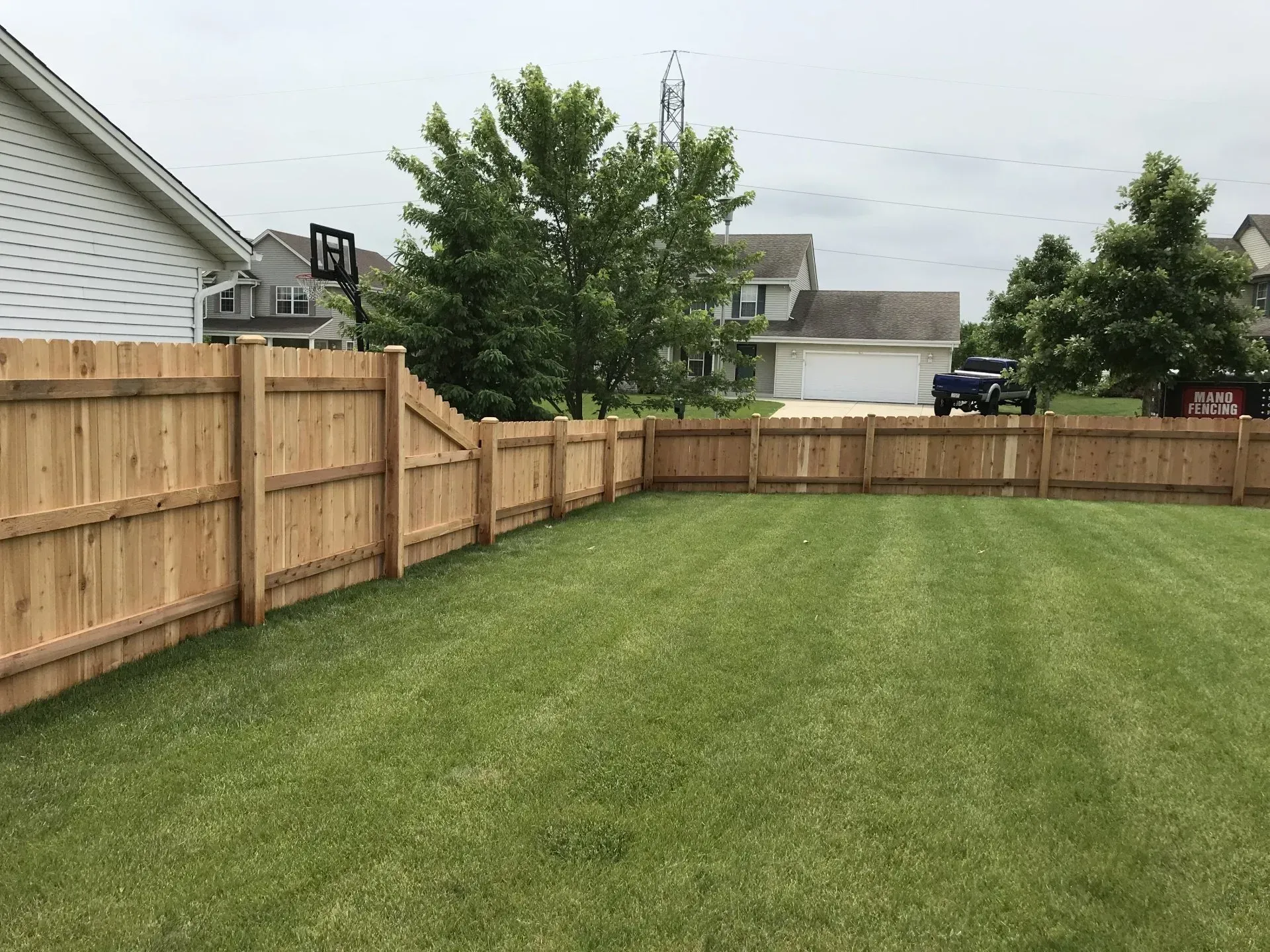 A view of a manicured green lawn enclosed by a new light-colored wooden privacy fence on a suburban lot.