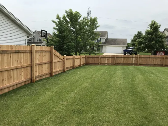 Freshly mowed backyard with a wooden privacy fence and neighboring houses under a cloudy sky