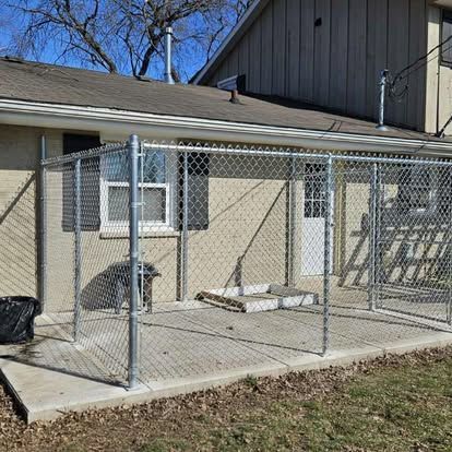 A fenced dog kennel on a concrete patio attached to the back of a beige house.
