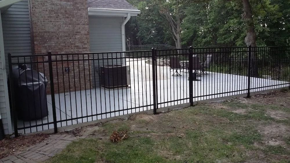 Black metal fence enclosing a concrete patio next to a house with a brick exterior.