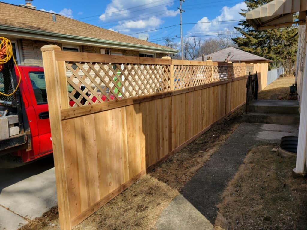 A newly installed wood fence with a lattice top along a gravel path next to a residential house and a red truck.