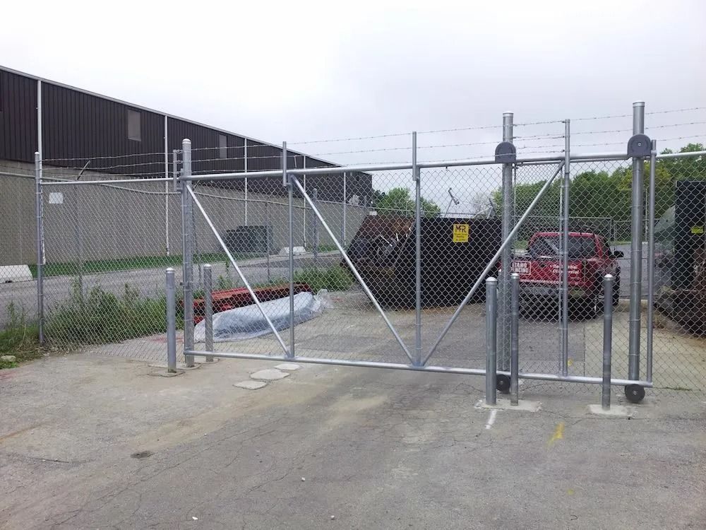 A chain-link sliding gate at an industrial facility entrance with a red vehicle parked inside.