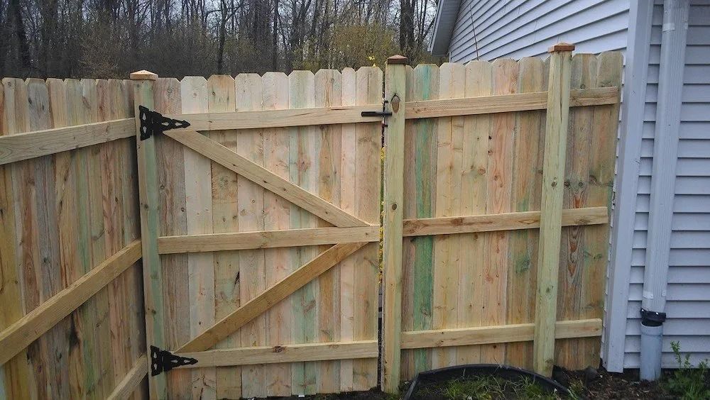 A wooden gate attached to a privacy fence next to a house with light-colored siding.