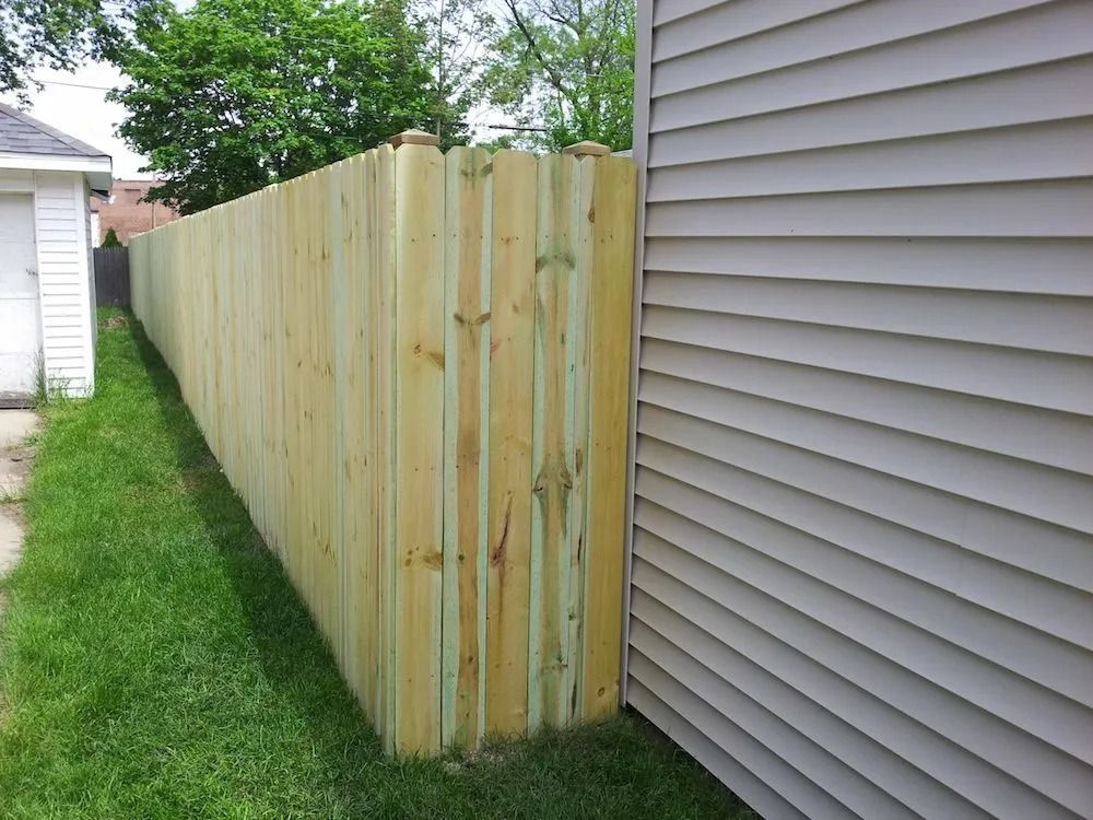 A new wooden privacy fence stands between a building with light gray siding and a grassy yard.