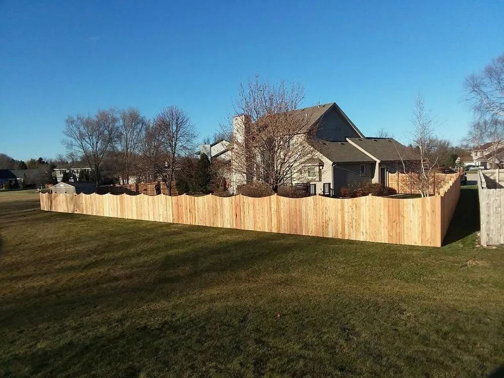 A wooden scalloped-top privacy fence surrounds the yard of a suburban home on a clear, sunny day.