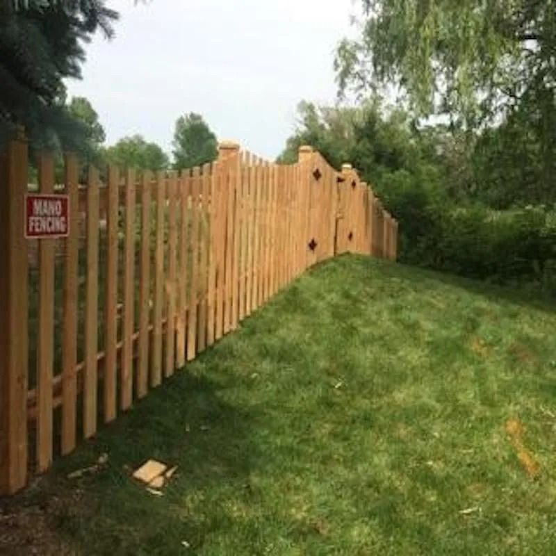 A wooden picket fence follows a grassy hill, with a gate and a red sign that reads 