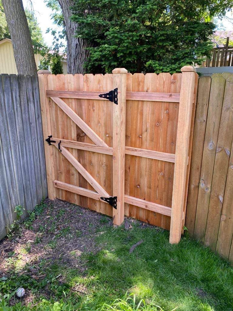 A newly installed cedar wood gate with black hinges and a latch set between two existing wooden fence sections.