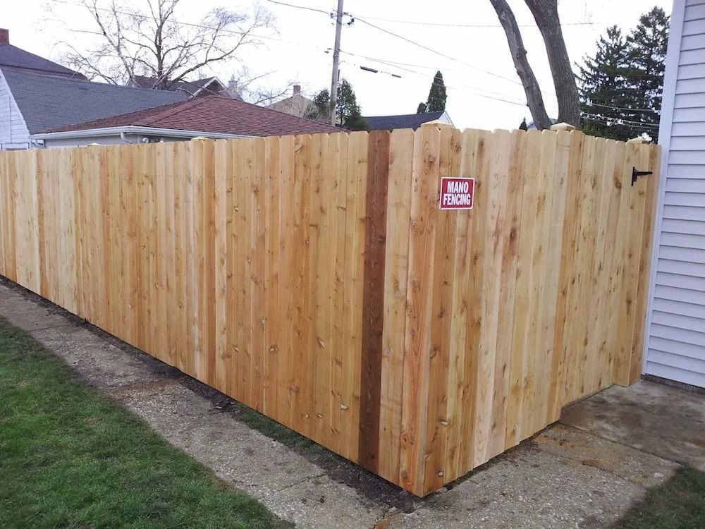 A new, light-brown wood privacy fence spans a grassy backyard next to a residential house.