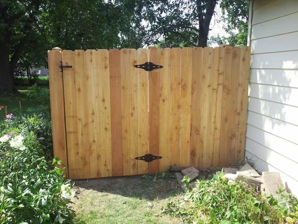 A new cedar wood privacy gate with black decorative strap hinges installed between a house wall and a garden area.
