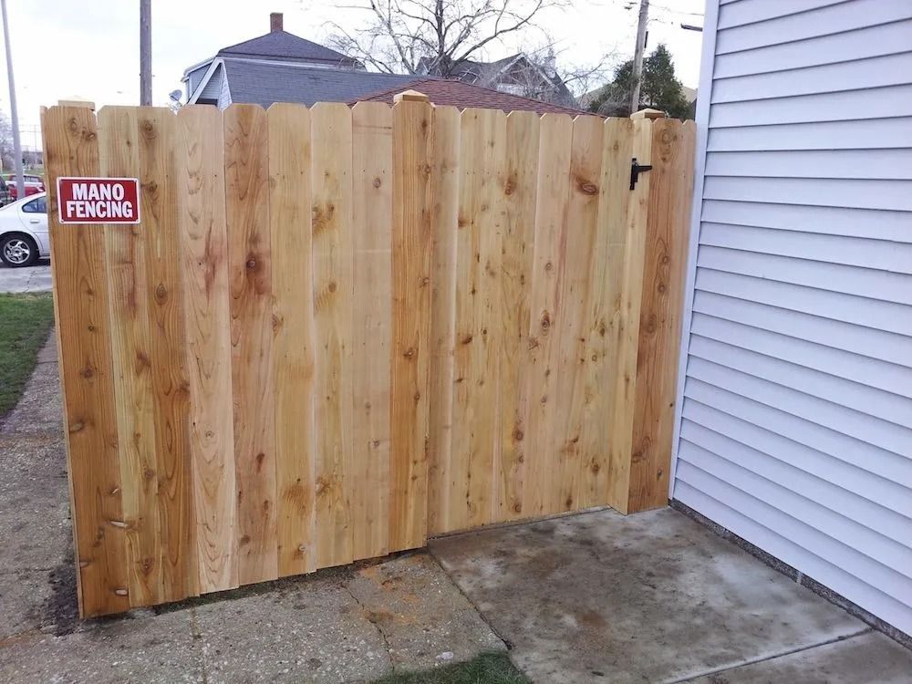 A newly installed light brown wooden privacy fence attached to the side of a white house, with a small red sign.