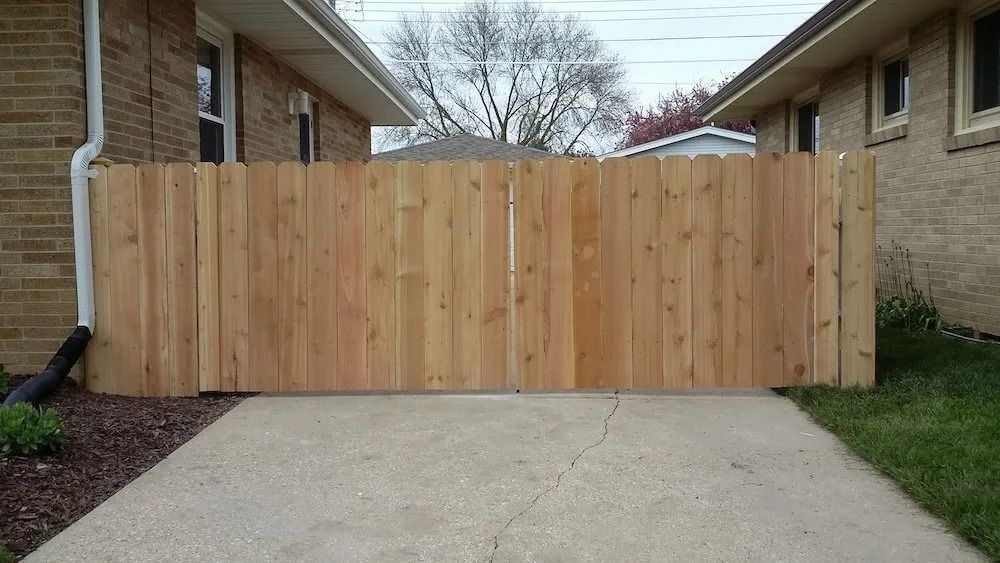 A new wooden fence gate installed between two brick houses on a concrete driveway.