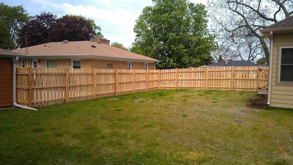 A newly installed wooden privacy fence spans a backyard between two residential houses.