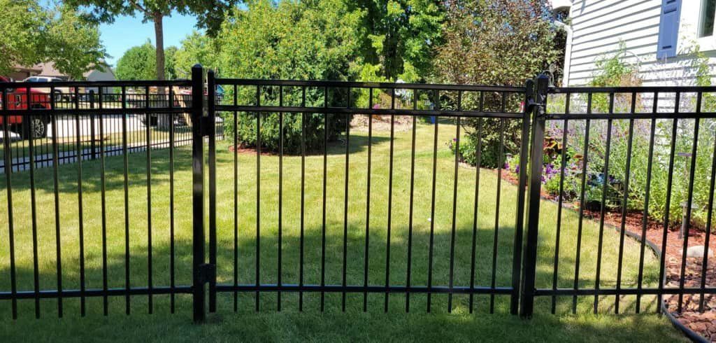 A black metal ornamental fence stands in a grassy yard near the side of a house.