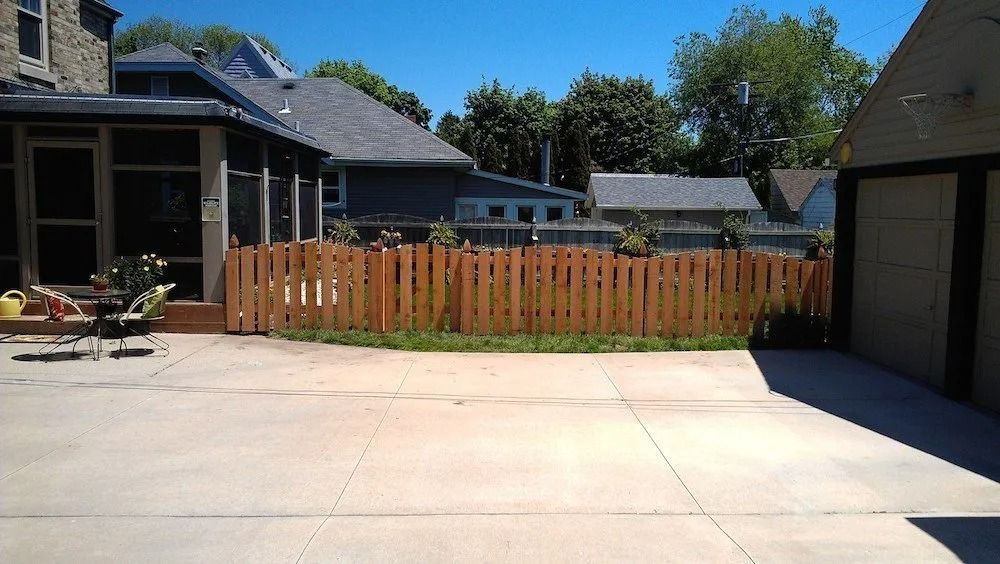 A patio area with a wooden fence separating the concrete driveway from a grassy yard, with a screened porch on the left.