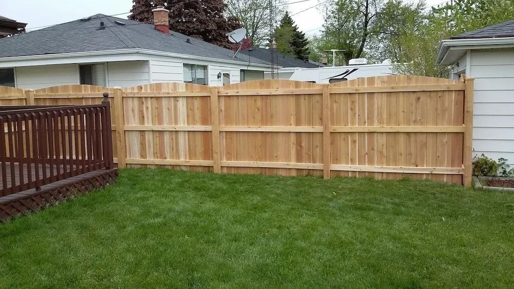 A backyard scene showing a new wooden fence installed along the property line next to a deck and house exterior.