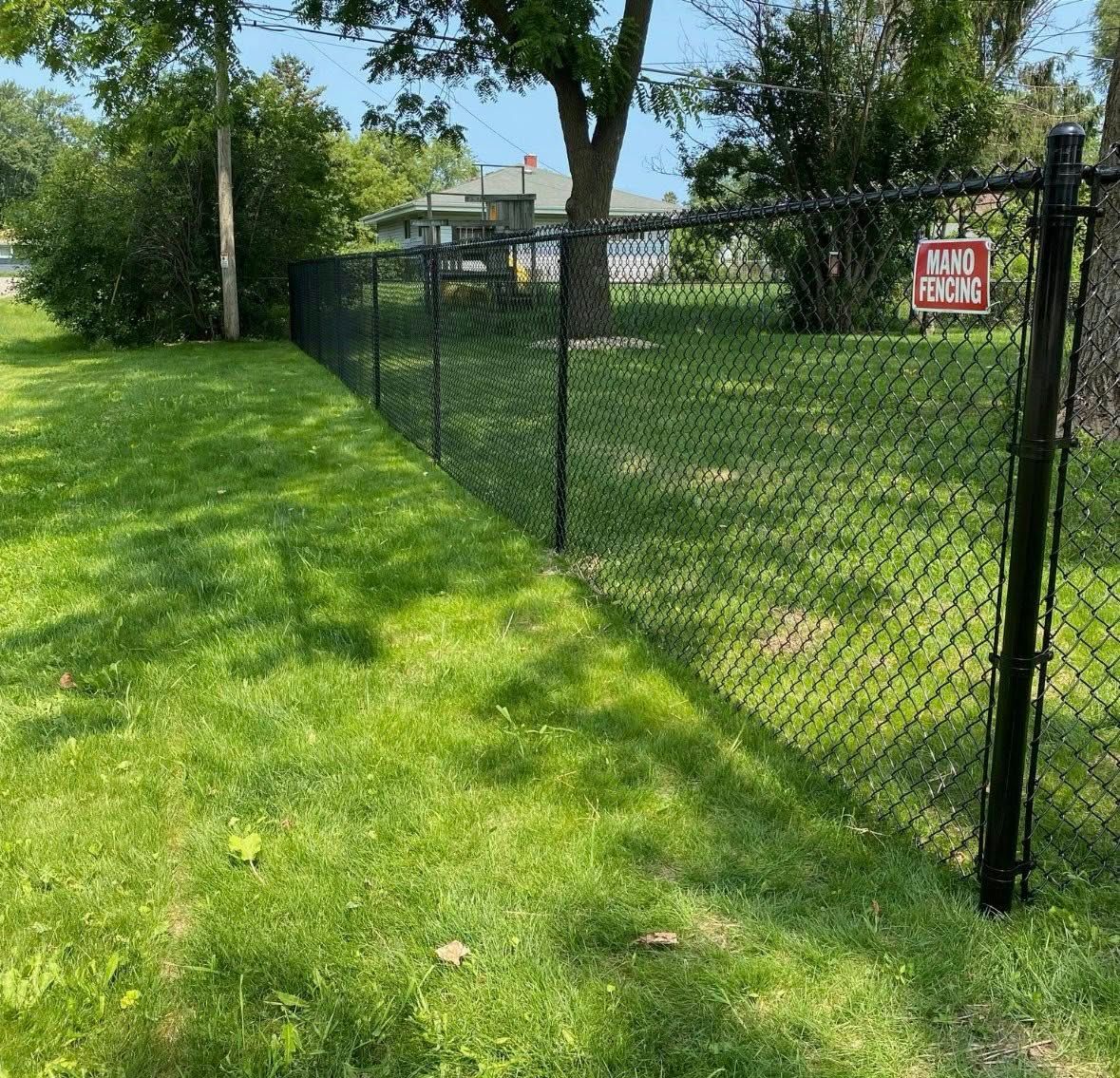 A black chain-link fence runs through a grassy lawn toward a small building in the background.