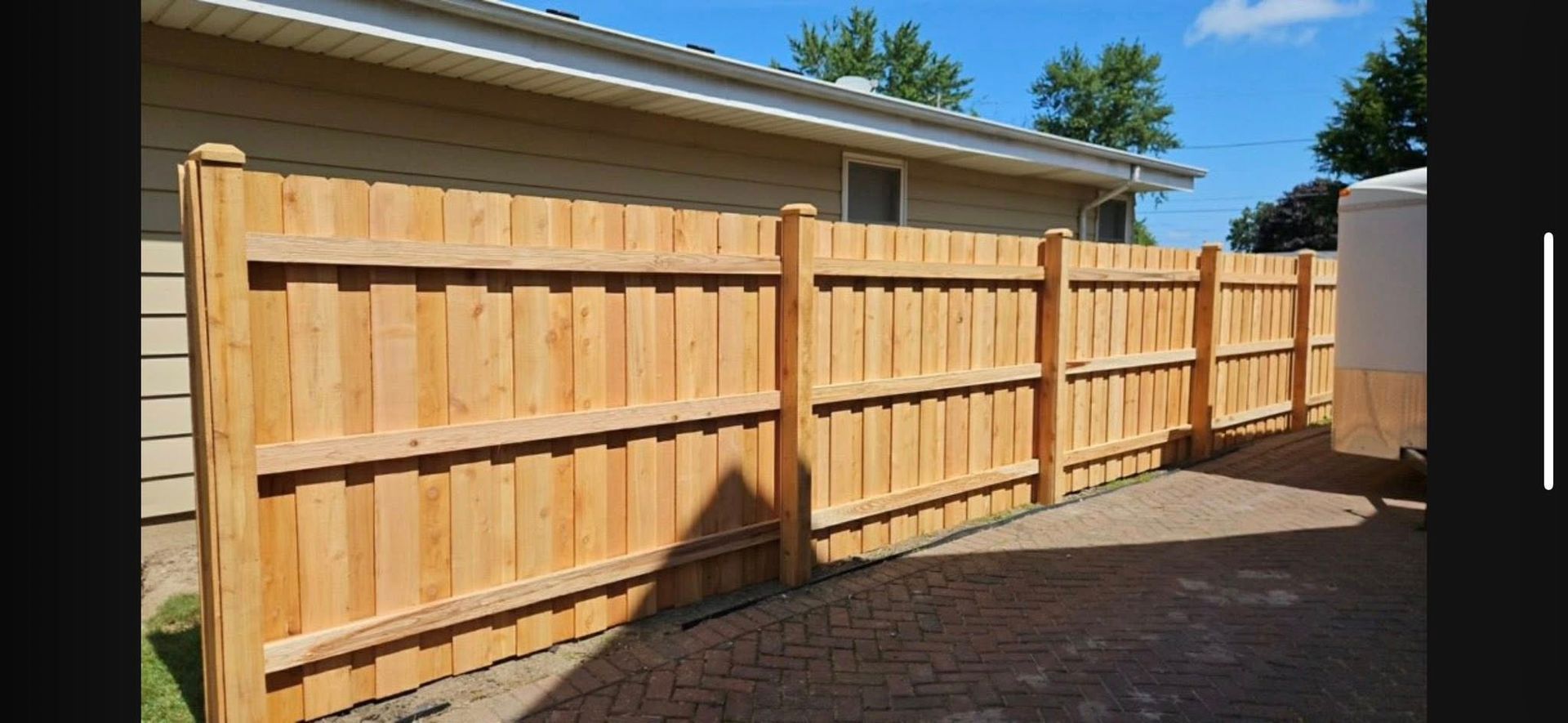 A wooden privacy fence standing on a paved surface next to a residential house.