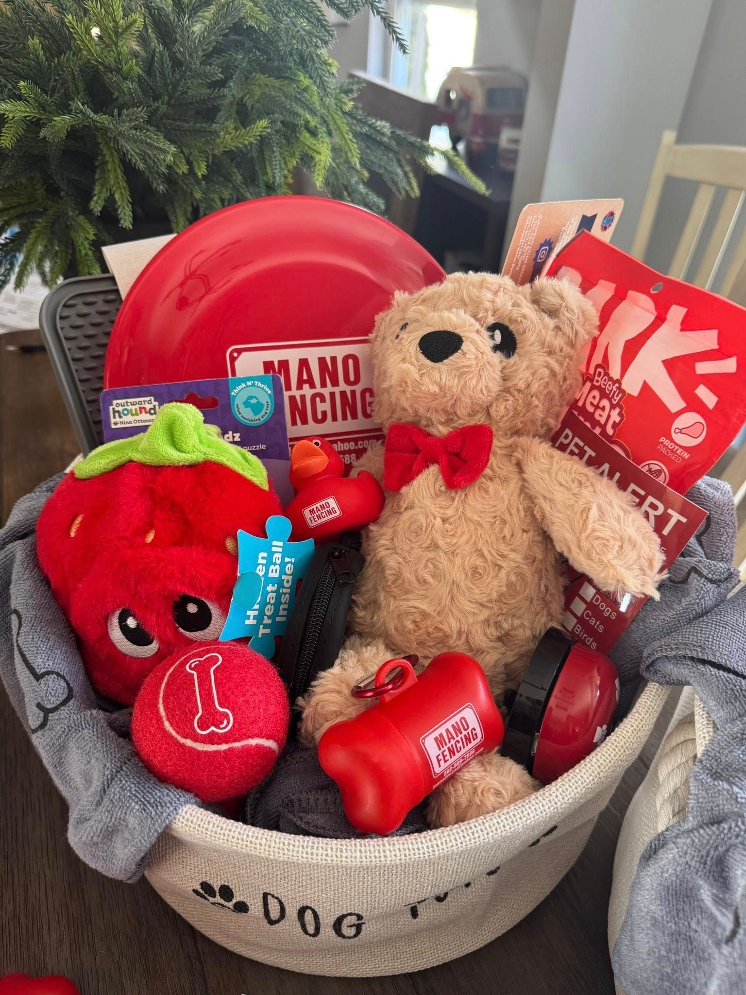 A woven basket filled with dog toys, a red frisbee, a plush bear, and dog treats on a wooden surface.