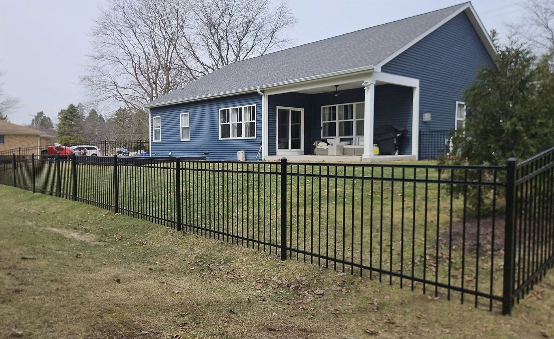 Blue house with white trim behind a black metal fence on a grassy lot