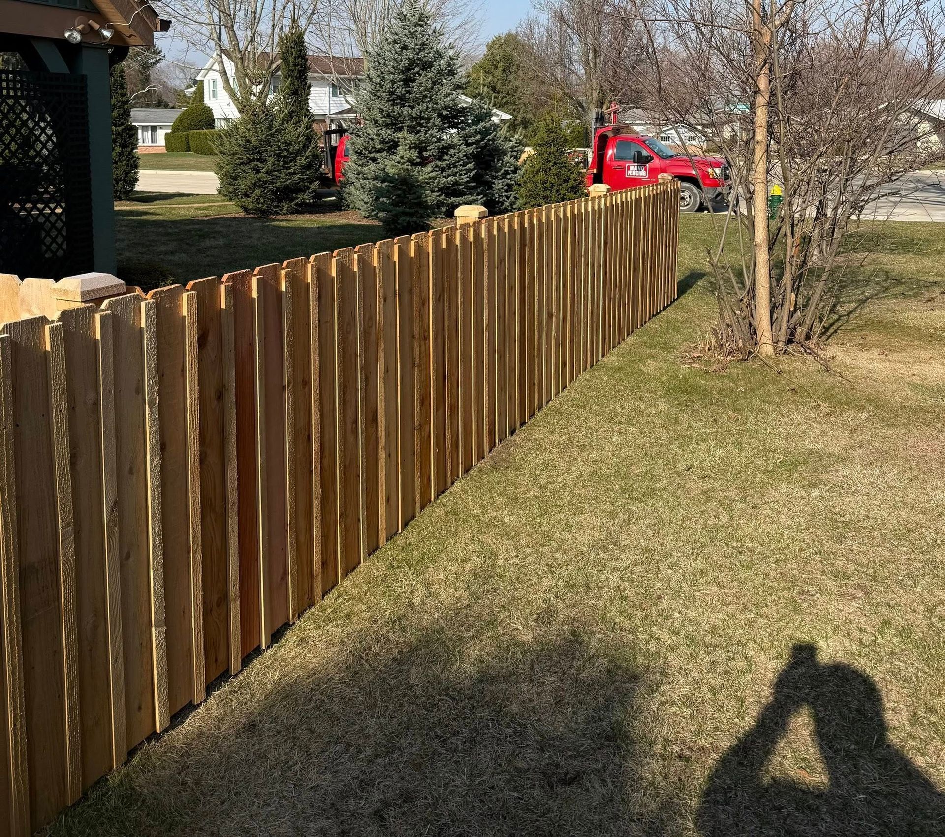 Wooden backyard fence beside a grassy yard, with a red truck and trees in the background.