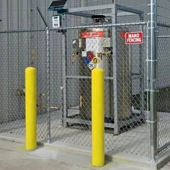 Chain-link fenced utility area with yellow bollards and red warning signs beside a building.