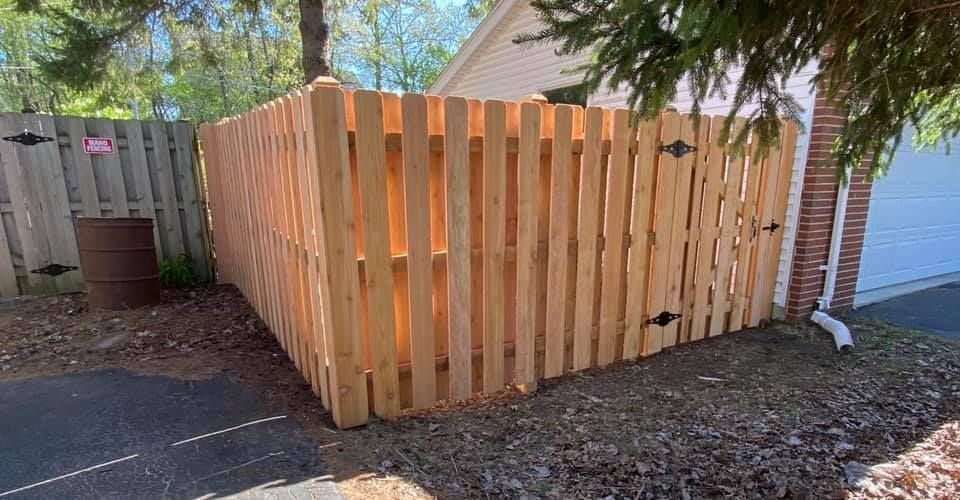 Wooden privacy fence enclosure beside a house, with a red barrel and gravel yard.
