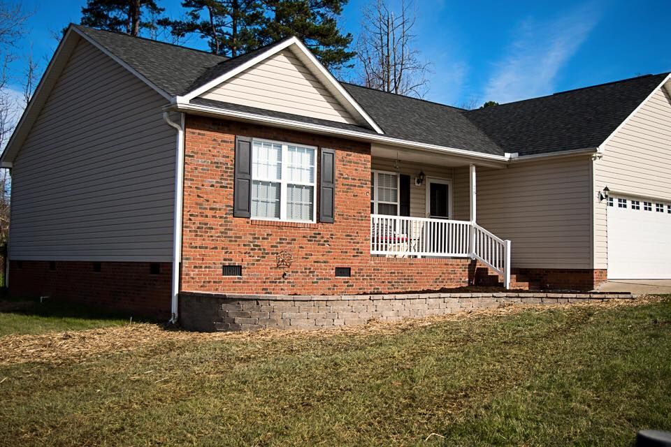 Brick and tan ranch house with a small porch, black shutters, and a retaining wall in front.