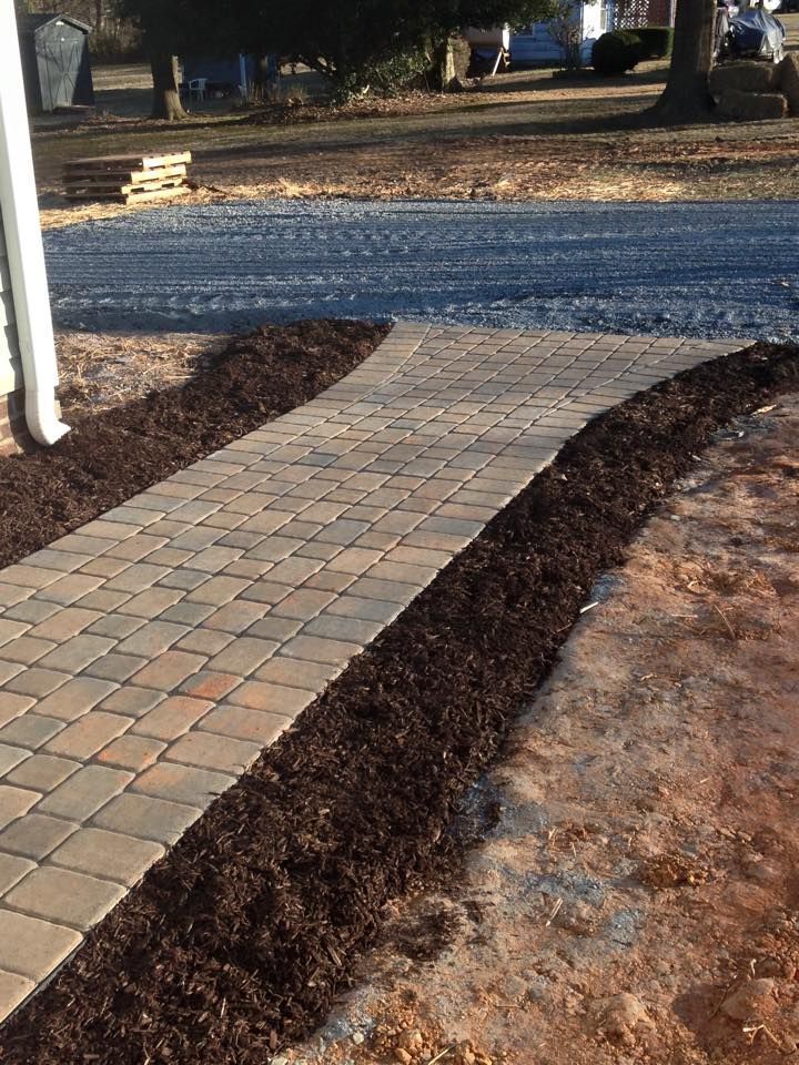 Brick walkway lined with dark brown mulch, leading from an unpaved driveway.