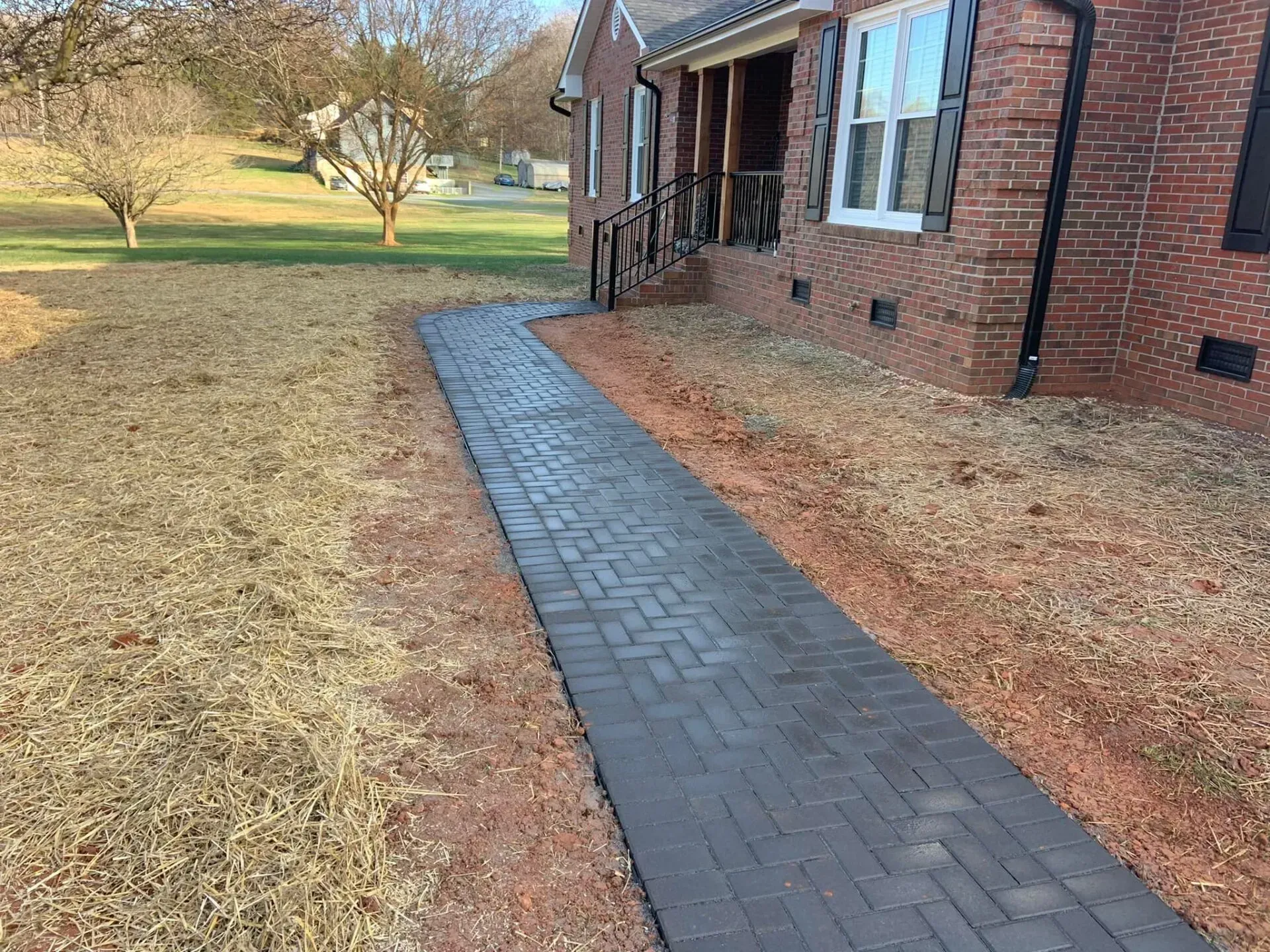 Brick pathway leading from the yard to the front door of a brick house. The yard has brown grass.