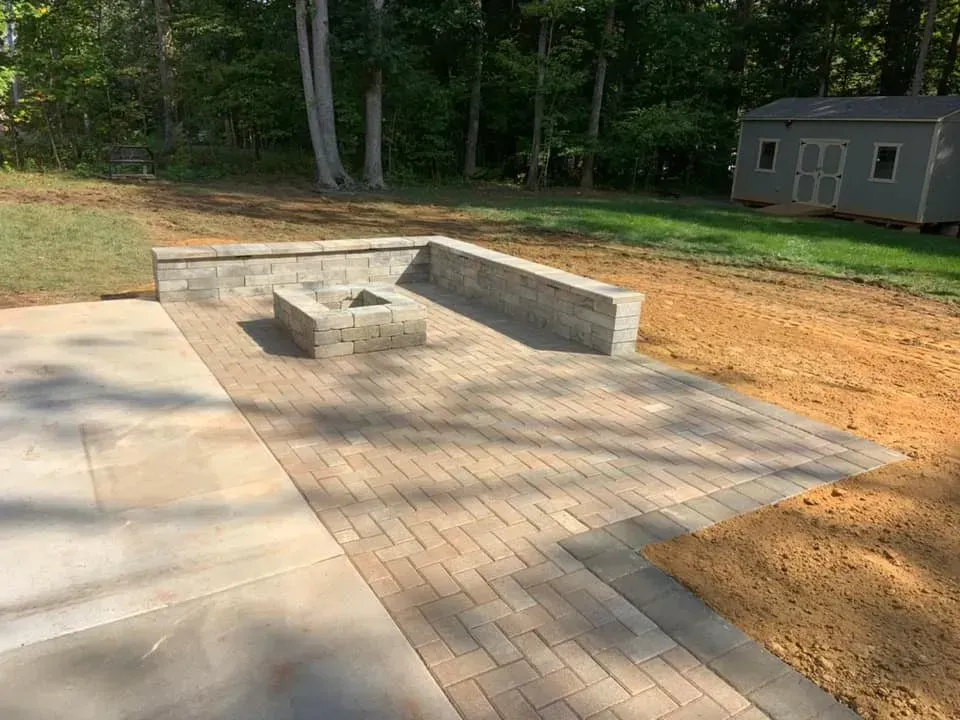A newly built patio with a fire pit, brick pavers, and retaining walls. A small shed is visible in the background.