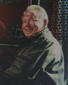 Smiling man in a dark jacket turning toward the camera indoors