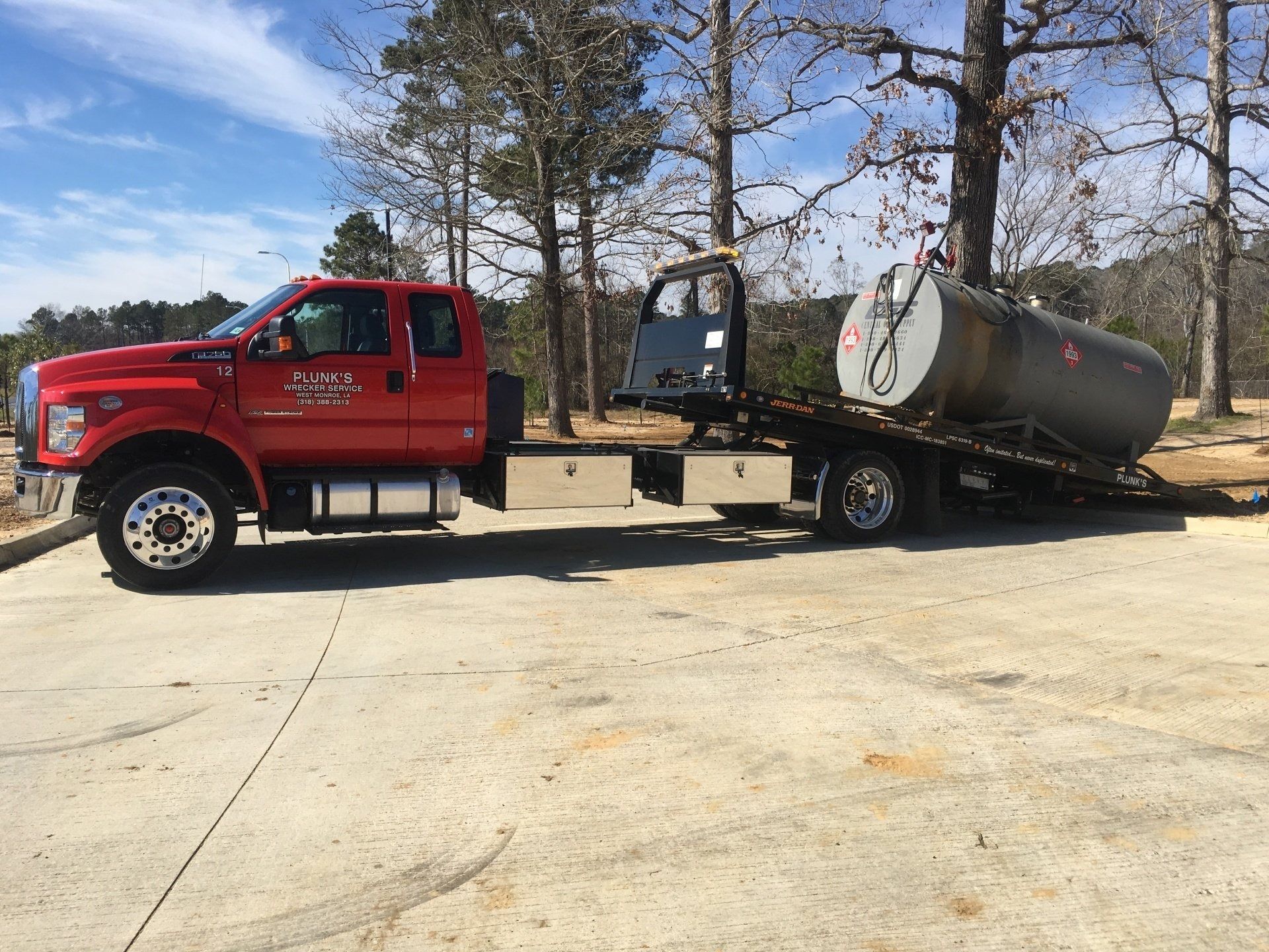 Red pickup truck hauling a large horizontal fuel tank on a trailer in a sunny outdoor lot