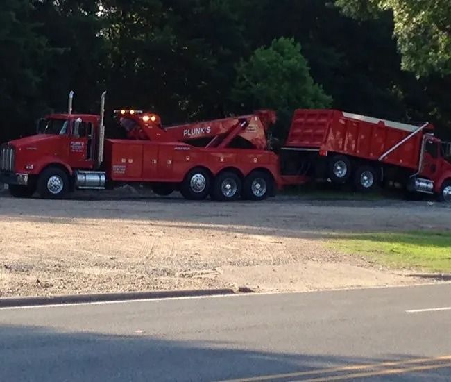 Red tow truck hauling a damaged red semi-trailer on a roadside shoulder.