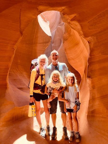 Family poses in a narrow, orange sandstone canyon. Light shines through opening.