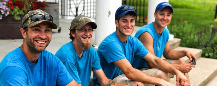 Four people in blue shirts and hats sit outside smiling, likely posing for the photo.