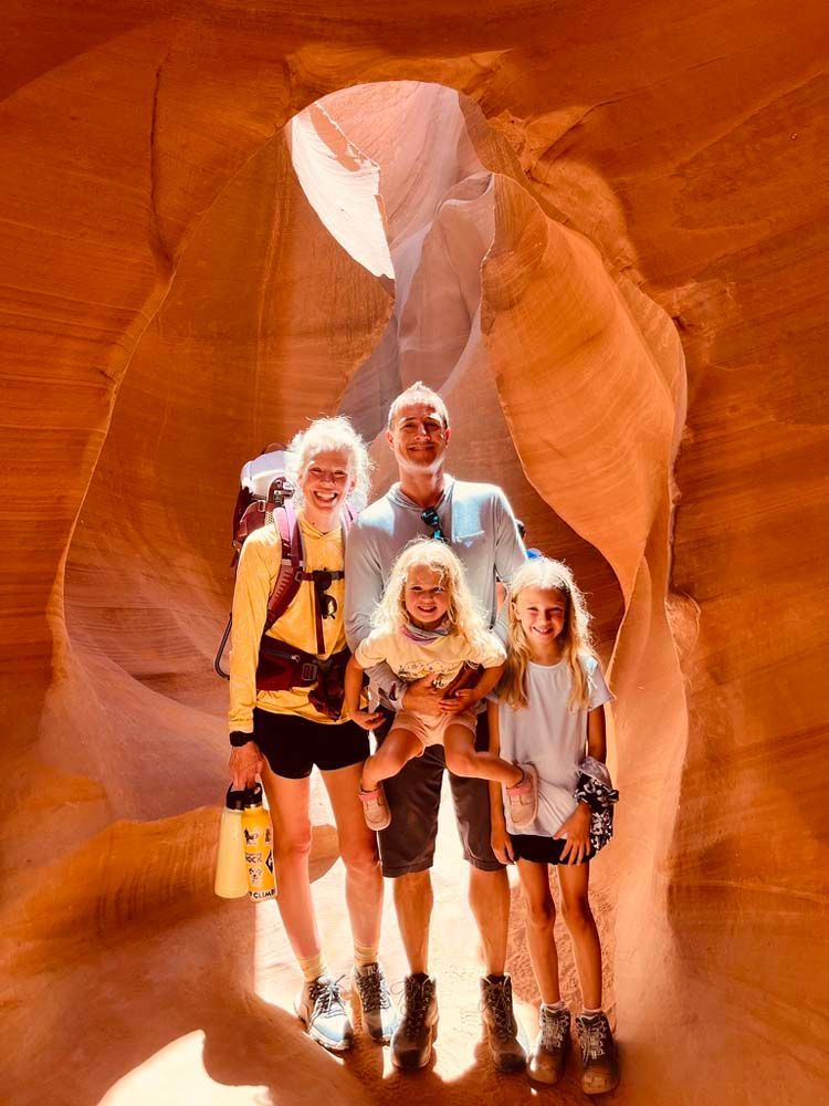 Family of five stands in a red-orange sandstone canyon. Natural light shines above.