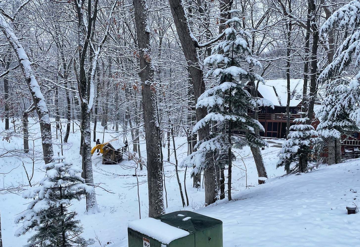 Snowy forest scene with cabin in background; excavator clearing snow.