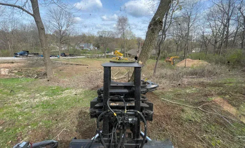 Heavy machinery with a tree shear clearing a wooded area.