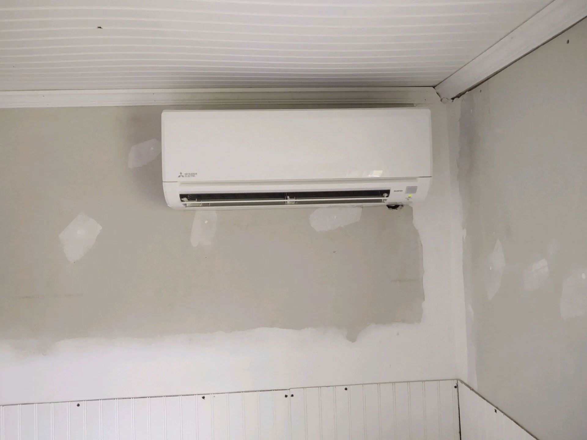 Wall-mounted white air conditioner above unfinished drywall in a room