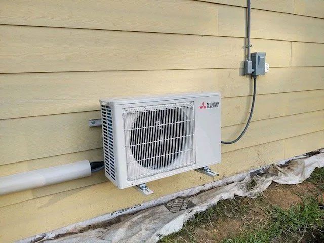 Outdoor wall-mounted air conditioner unit beside a beige house wall and utility conduit