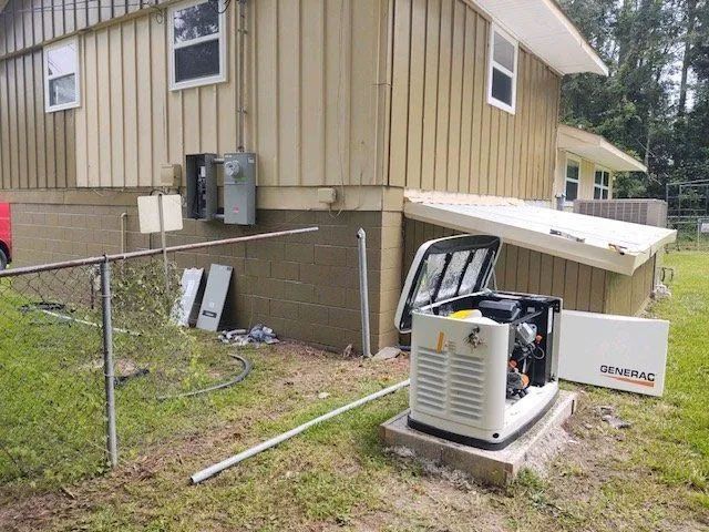 Generator beside a beige house with an open panel, near a chain-link fence and AC units.