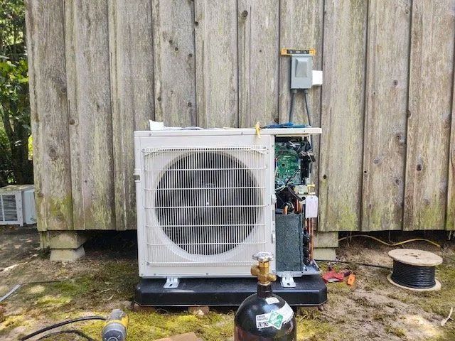 Outdoor air conditioner unit beside a weathered wooden shed, with exposed components and tools nearby